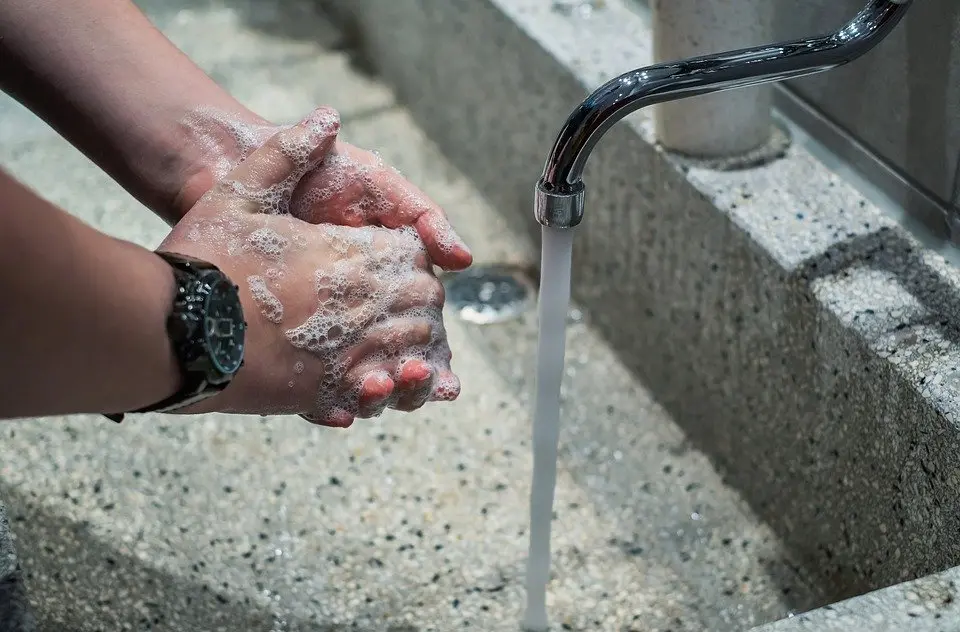 Två händer som tvättas med löddrande tvål intill en kran med rinnande vatten.